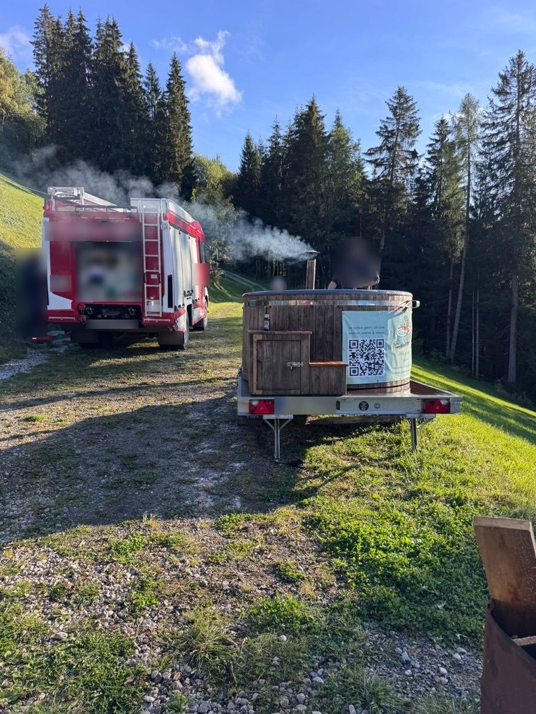 Mobiler Holz-Whirlpool mit rauchendem Holzofen neben einem Feuerwehrauto – im Einsatz bei einer Vereinsfeier